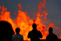 Onlookers stand on a lava flow to watch lava gush out of a fissure, in the Leilani Estates near Pahoa, Hawaii, U.S., May 26, 2018. REUTERS/Marco Garcia