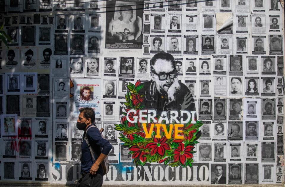 A man walks past a wall of photographs of war victims and an image of Msgr. Juan Jose Gerardi