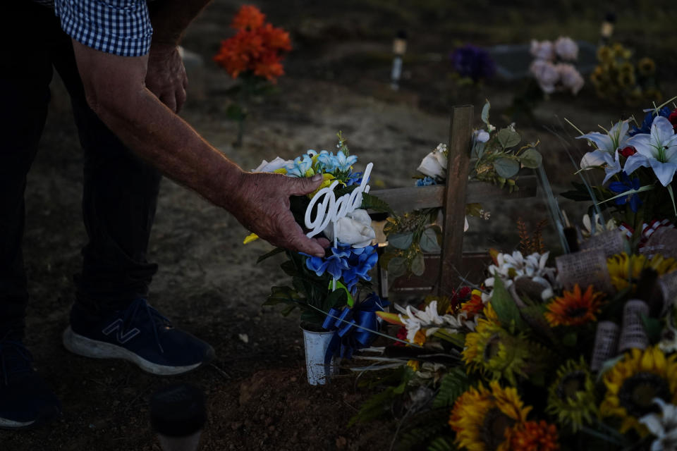 Larry Guess adjusts a flower bouquet with a "Dad" insert on his son's David's grave on Thursday, June 23, 2022, in Athens, Ala. David Guess was killed by gun violence in March. According to the police, Guess was shot with a handgun and burned in a wooded area with tires piled on his body and set on fire. (AP Photo/Brynn Anderson)