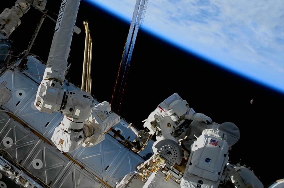 NASA astronaut Stephen Bowen (right) and UAE astronaut Sultan AlNeyadi work on an antenna assembly as the Earth and moon hang overhead outside the International Space Station.