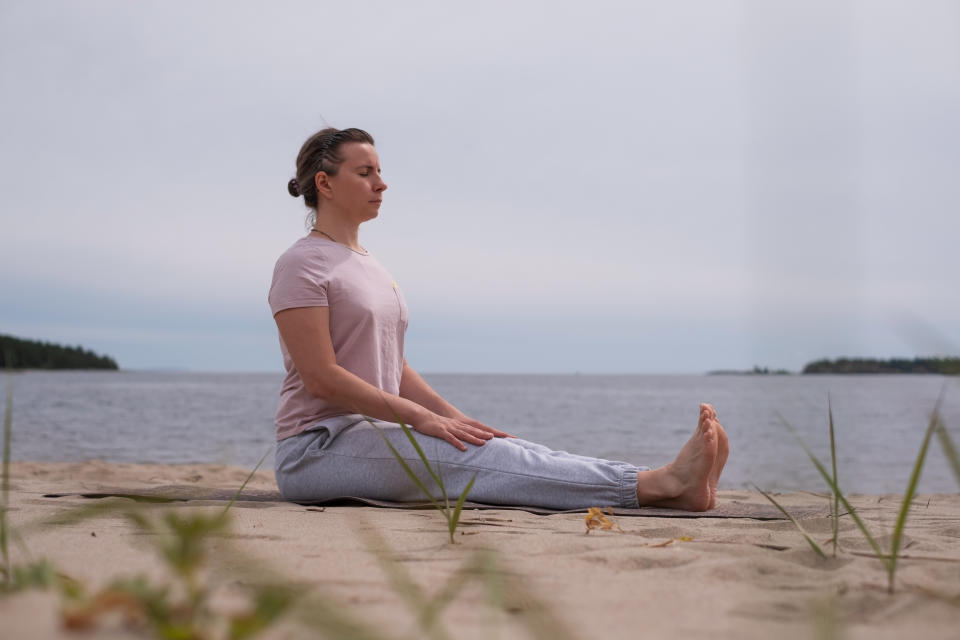 Young sporty woman practicing yoga, doing Dandasana pose, working out on the beach