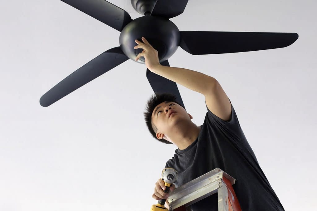 A man installs a ceiling fan. 