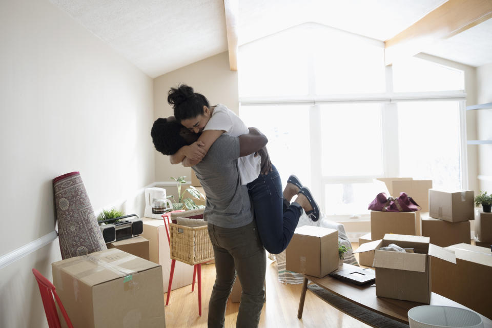 Enthusiastic, affectionate couple hugging in new home, unpacking cardboard boxes