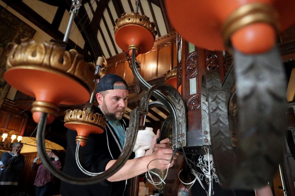 Tom Treadaway of Halper Lighting Solutions is framed by some of the 28 chandelier arms as he helps put the restored piece back together in the great room at Stan Hywet Hall and Gardens.