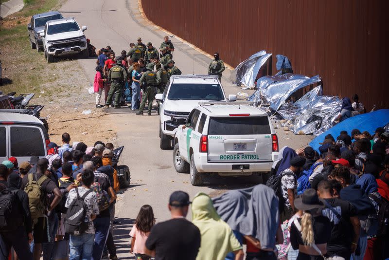 U.S border patrol interact with migrants who have gathered between border fences of U.S. and Mexico in California