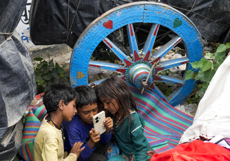 A group of nomadic children look at a mobile phone next to a bullock cart on a hot summer afternoon in Lalitpur district in northern Uttar Pradesh state, India, Sunday, June 18, 2023. Swaths of two of India's most populous states are under a grip of sever heat leaving dozens of people dead in several days as authorities issue a warning to residents over 60 and others with ailments to stay indoors during the daytime. (AP Photo/Rajesh Kumar Singh)