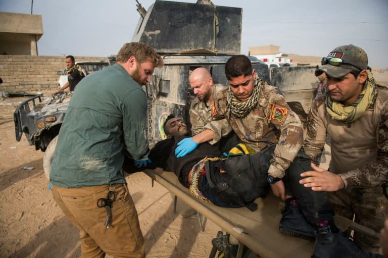 Frontline medics help carry an Iraqi soldier hit by sniper fire out of their vehicle at an outdoor field clinic in the Samah neighbourhood of Mosul on November 15, 2016