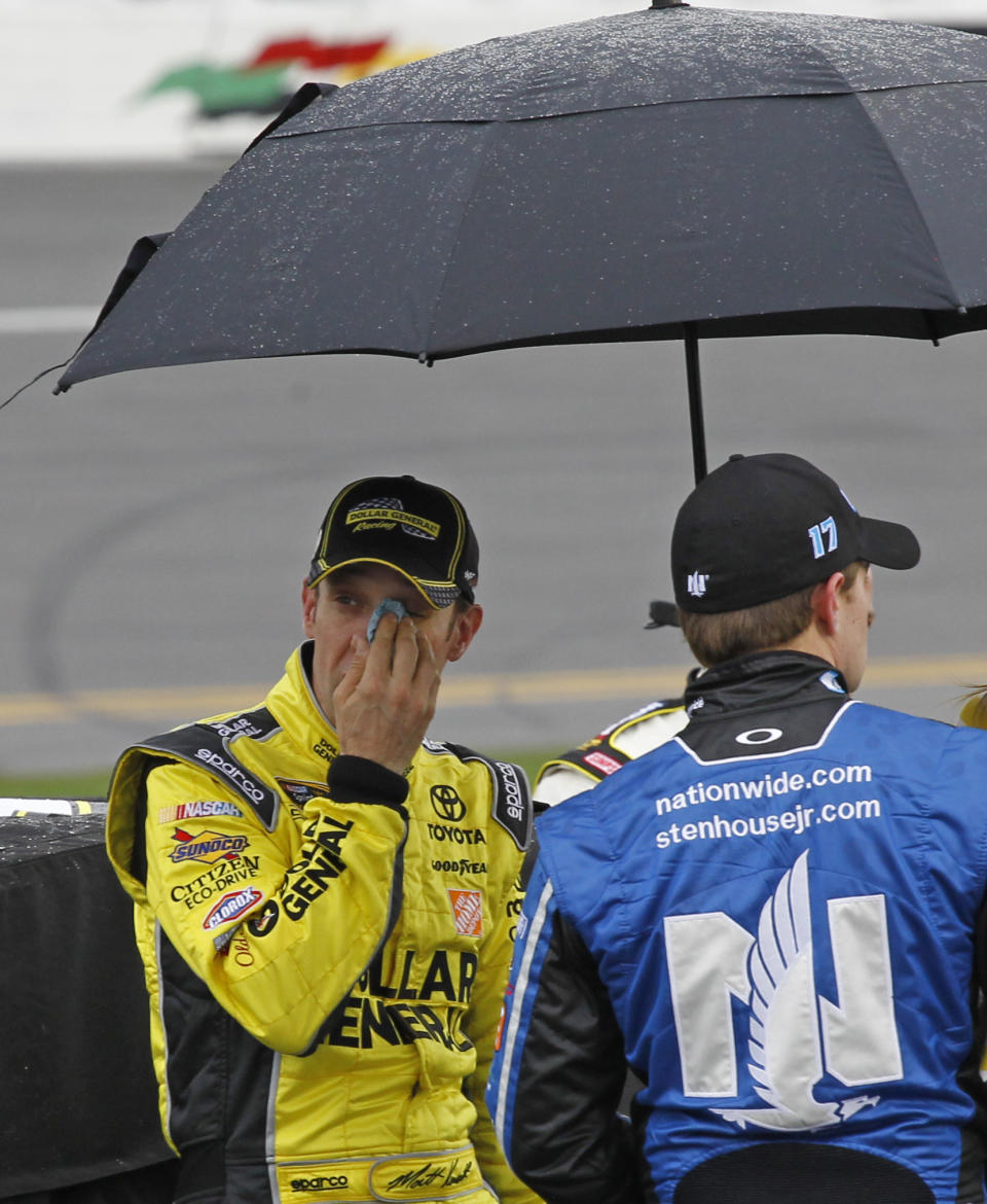 Matt Kenseth, left, looks out from under an umbrella as he stands near his car during a rain delay in the NASCAR Daytona 500 Sprint Cup series auto race at Daytona International Speedway in Daytona Beach, Fla., Sunday, Feb. 23, 2014. (AP Photo/Terry Renna)