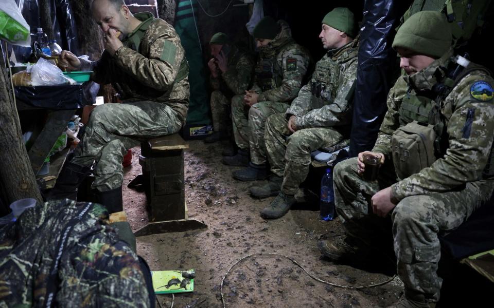 Ukrainian soldiers sit with dead mice on the floor of a trench dugout