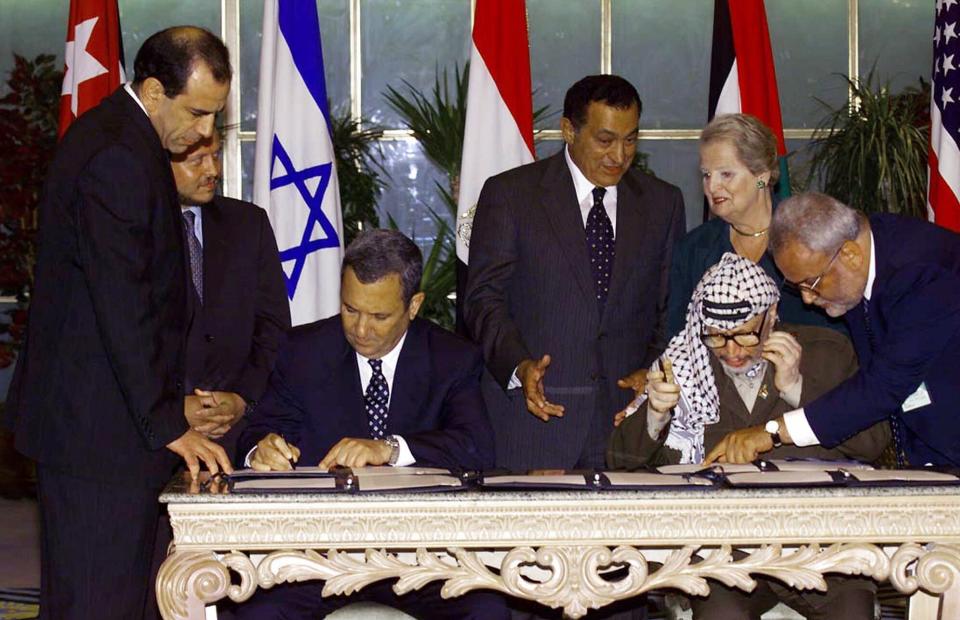 FILE - In this Sept. 5, 1999 file photo, Palestinian leader Yasser Arafat, seated right, consults with Saeb Erekat, right, as Israeli Prime Minister Ehud Barak, seated left, sign a land-for-security agreement in the Egyptian resort town of Sharm el-Sheikh as U.S. Secretary of State Madeleine Albright, background right, Egyptian President Hosni Mubarak, center background, and Jordan's King Abdullah II, left background, look on. Erekat, a veteran peace negotiator and prominent international spokesman for the Palestinians for more than three decades, died Tuesday, Nov. 10, 2020. He was 65. (AP Photo/Dimitri Messinis, File)