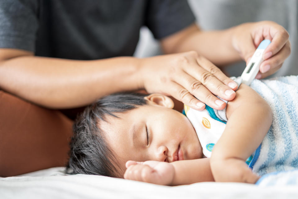 Young Asian single Mother with her baby at home with care using fever thermometer electronic