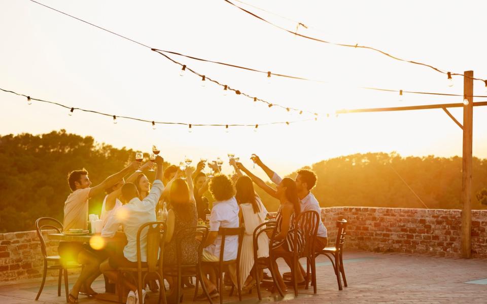 Friends toasting drinks during social gathering - Getty