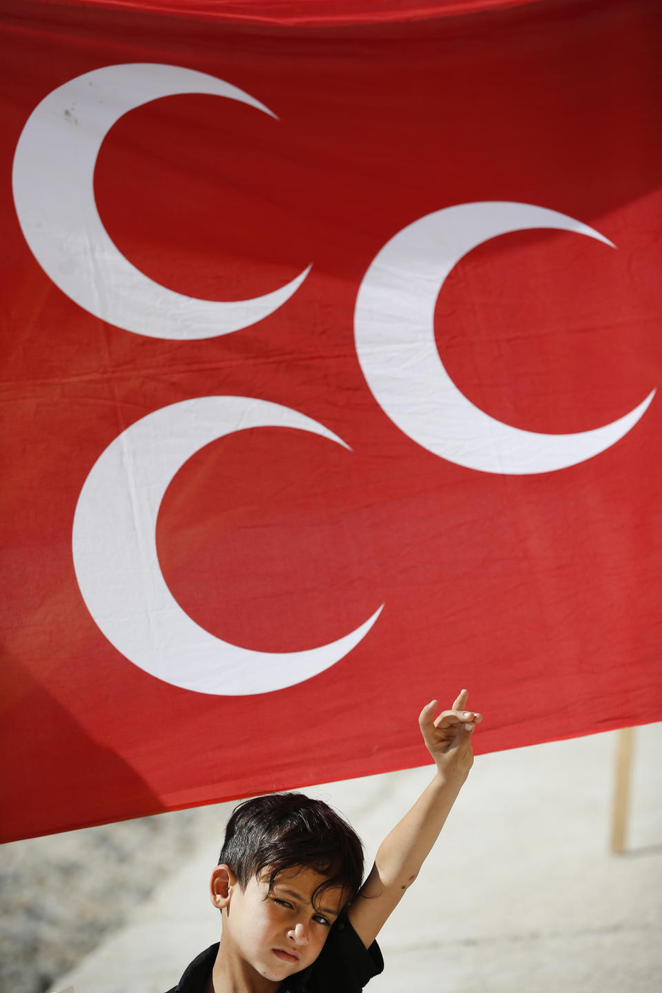 FILE-In this Tuesday, Oct. 8, 2019 file photo a child flashes a hand gesture representing the Turkish far-right grey wolves organisation as he stands by a flag of Turkey's Nationalist Movement Party (MHP) at the Turkish side of the border between Turkey and Syria, in Akcakale, Sanliurfa province, southeastern Turkey. Since Turkey announced its incursion into neighbouring Syria to clear out Kurdish fighters last week, patriotic sentiment has run high, with national emblems being proudly displayed. (AP Photo/Lefteris Pitarakis, File)