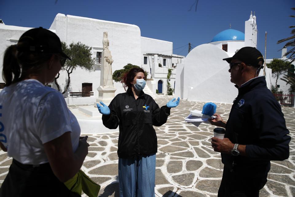 In this Monday, May 25, 2020 photo, a doctor of the Public Health Organization (EODY), center, speaks with the members of the non-for-profit Organization Symplefsi after she has tested the local residents for the new coronavirus, on the Aegean Sea island of Sikinos, Greece. Using dinghies, a GPS, and a portable refrigerator, state doctors have launched a COVID-19 testing drive on islands in the Aegean Sea ahead of the holiday season. The first round of testing was completed after trips to the islands of Milos, Kimolos, Folegandros, and Sikinos. (AP Photo/Thanassis Stavrakis)