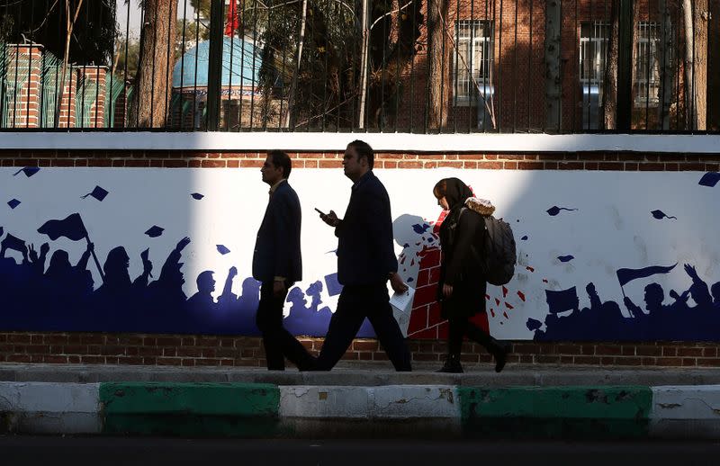 People walk past an Anti US mural on the former US embassy's wall in Tehran