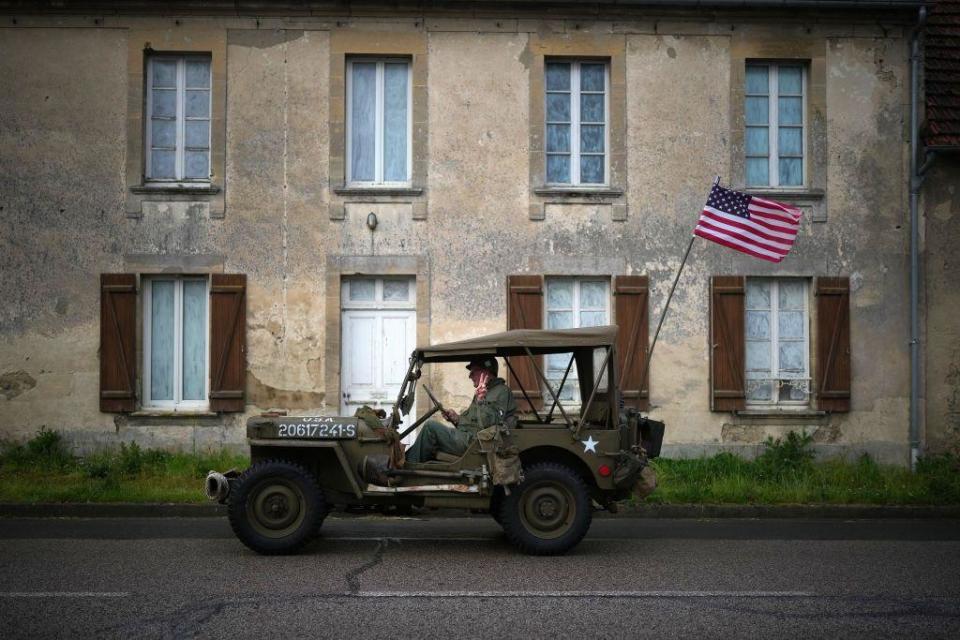 A man gives a victory sign as he drives a World War Two US Jeep through Colleville-sur-Mer, France