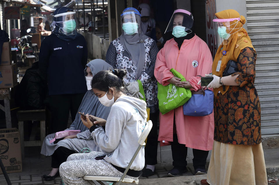 Health Ministry officials wearing protective gears, standing, look on as people wait to have their nasal swab samples collected during a mass test for the new coronavirus at a market in Jakarta, Indonesia, Thursday, June 25, 2020. (AP Photo/Tatan Syuflana)