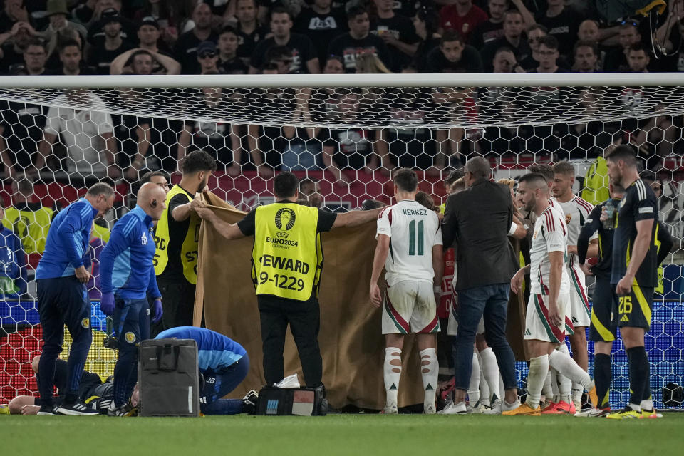 Stewards hold a blanket to protect the privacy of Hungary's Barnabas Varga as he gets medical treatment after a collision during a Group A match between Scotland and Hungary at the Euro 2024 soccer tournament in Stuttgart, Germany, Sunday, June 23, 2024. (AP Photo/Matthias Schrader)