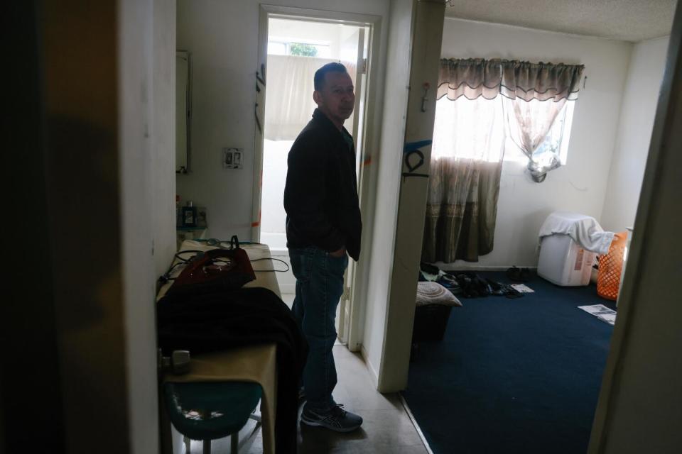 A man standing in an apartment outside a room with a dark-blue carpet