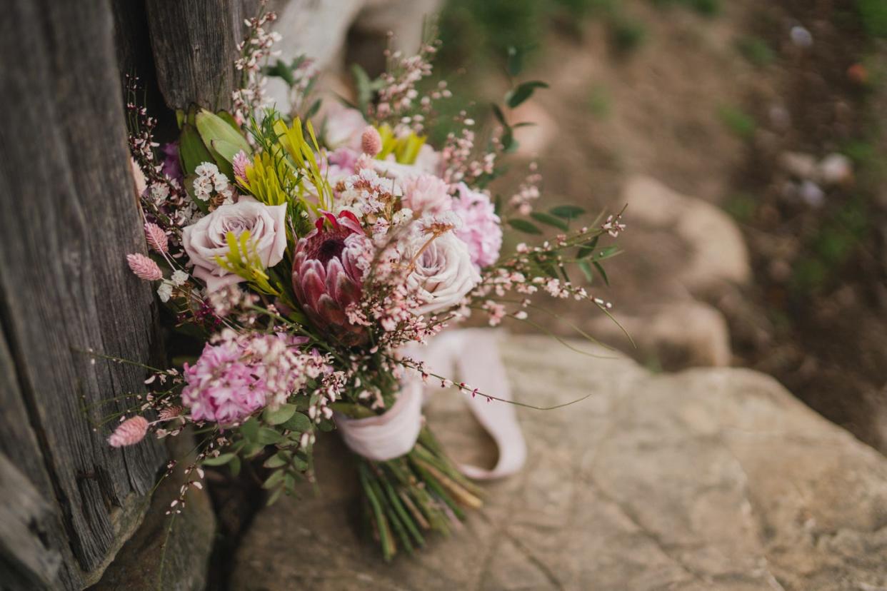 beautiful bridal bouquet of purple and pink flowers with lace ribbons standing on the stone near an old wooden house in the mountains