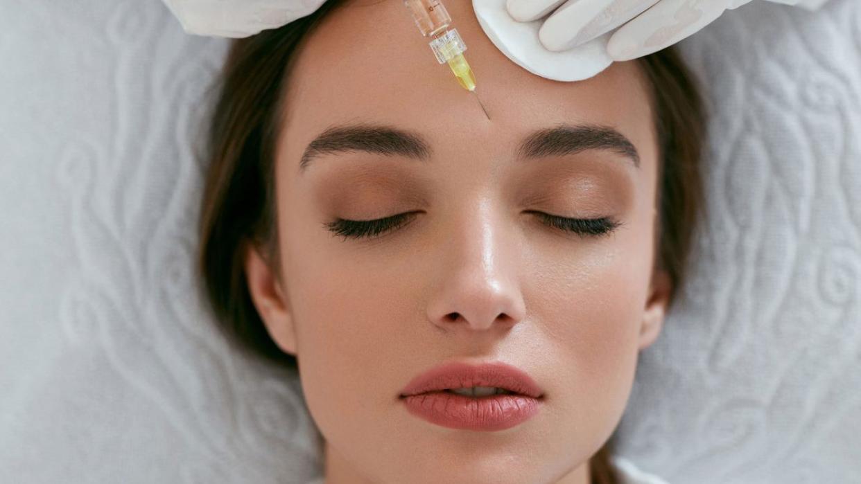 Young woman receiving facial filler injection by syringe