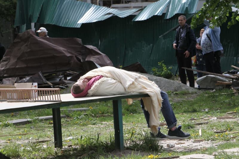 A man wrapped in a blanket lies on the table for table tennis at an apartment block that was partially destroyed by the Russian missile attack on Dnipro. -/Ukrinform/dpa