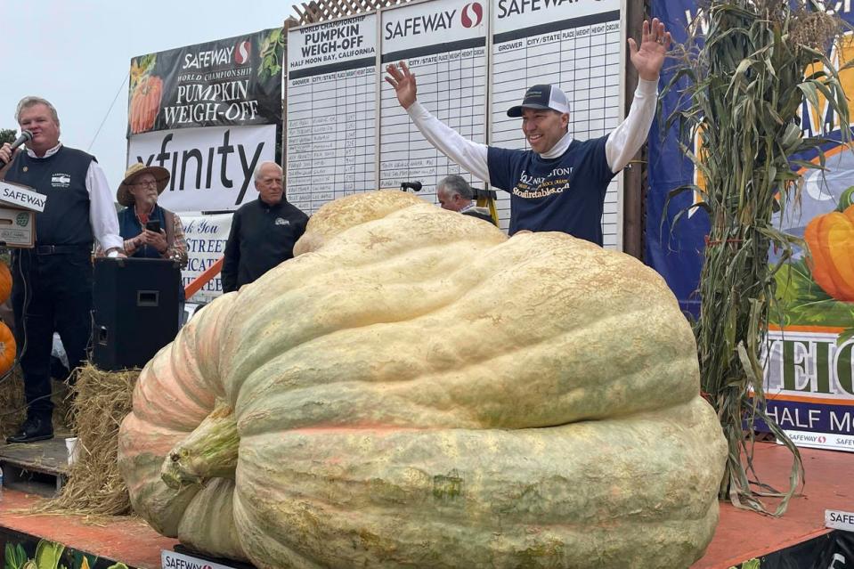 Travis Gienger from Anoka, Minn., stands behind his winning pumpkin at the 49th World Championship Pumpkin Weigh-Off in Half Moon Bay, Calif., on Oct. 10, 2022.