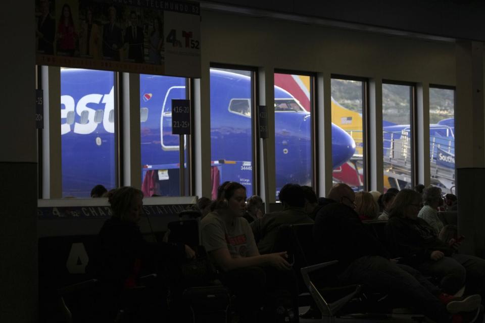 Passengers wait in an airport terminal and a Southwest Airlines plane is parked behind the windows.