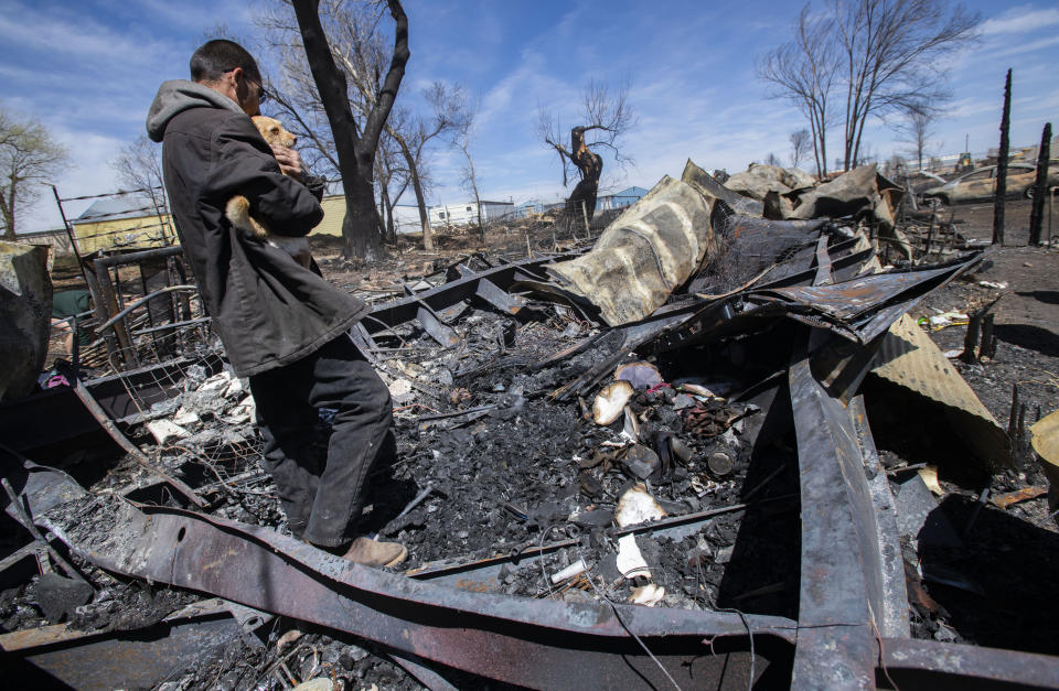 FILE - Savino Sanchez holds his mother-in-law's dog as he and his family search through the remains of their home in Monte Vista, Colo., April 22, 2022, after a fire fueled by high winds Wednesday burned 17 structures and displaced six families. The family lost everything except the clothes on their backs, two dogs and their cat. (Christian Murdock/The Gazette via AP, File)