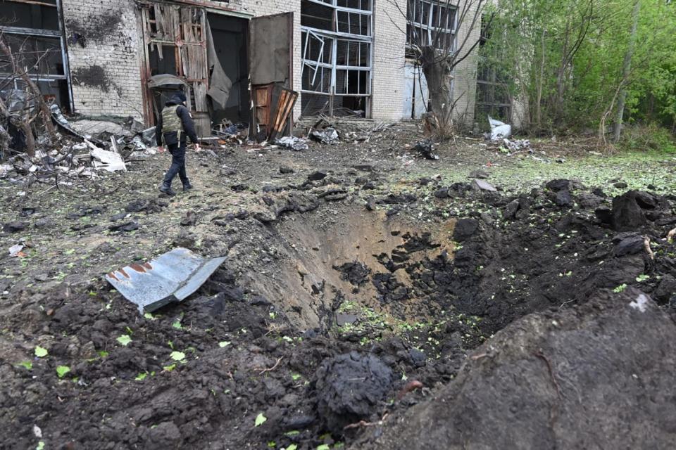 A law enforcement officer walks by a crater in Ukraine.