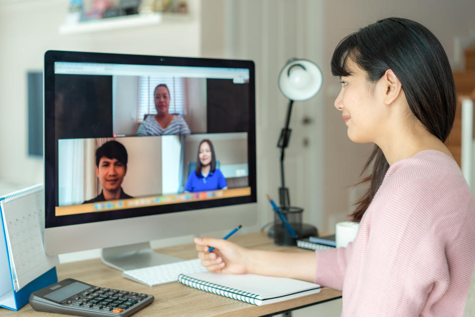 Back view of Asian business woman talking to her colleagues about plan in video conference. Multiethnic business team using computer for a online meeting in video call. Group of people smart working from home.