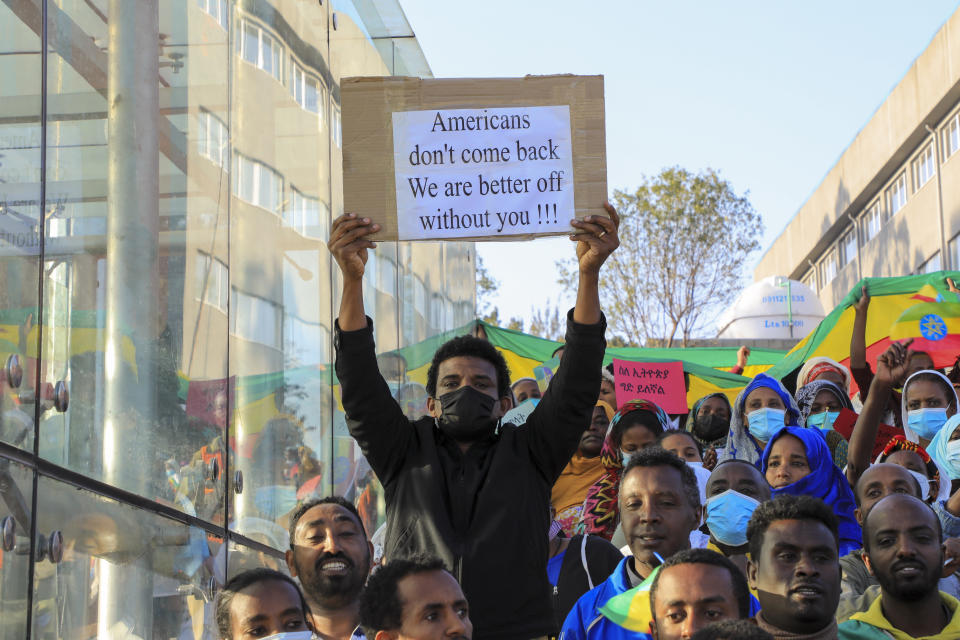 A man holds a placard referring to a recent decision by the US to order non-emergency government employees and their families to leave Ethiopia and urging other U.S. citizens that they should "depart now", as people gather at a rally organized by local authorities to show support for the Ethiopian National Defense Force (ENDF), at Meskel square in downtown Addis Ababa, Ethiopia Sunday, Nov. 7, 2021. (AP Photo)