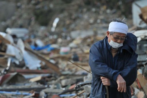 A man rests on a walking stick surrouned by debris in the devastated town of Rikuzentakata in Iwate prefecture