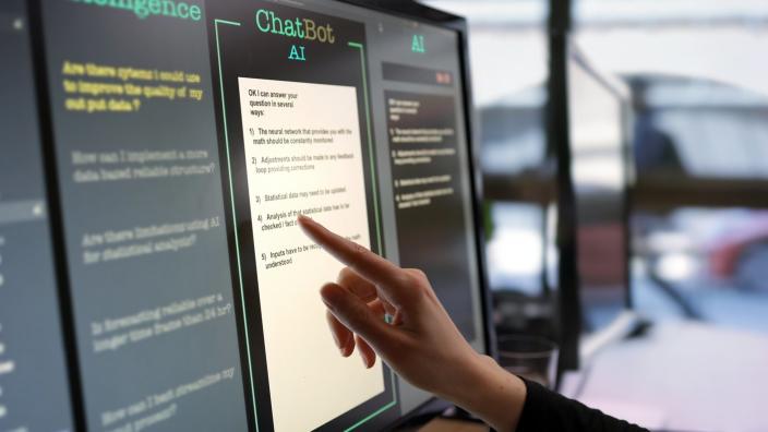 A finger points to a screen displaying  a chatbot.