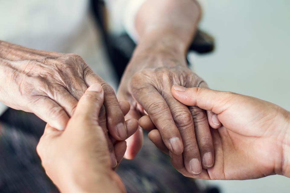 A person holds the hands of their elderly relative