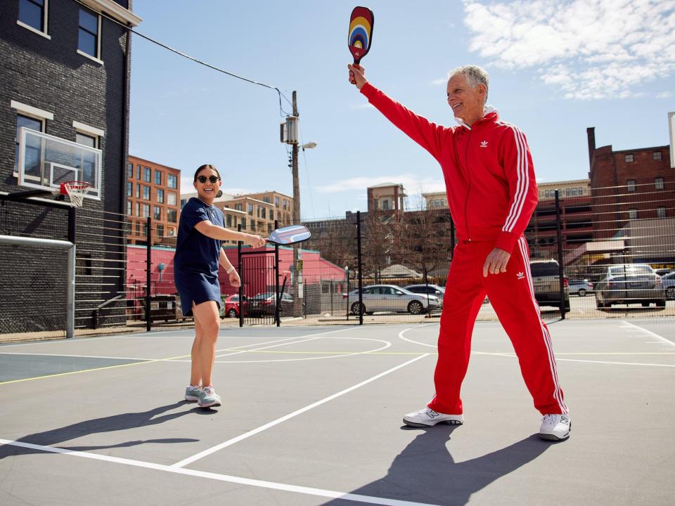 Child and man play pickleball on court in city neighborhood