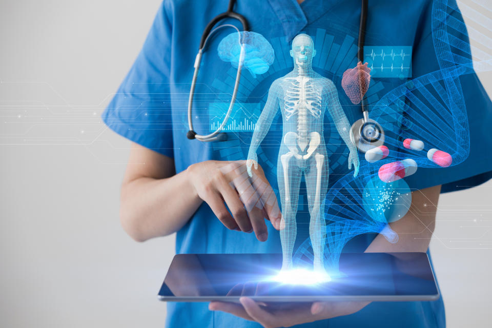 A doctor in scrubs holding a tablet that's projecting a holographic image of a transparent human body.