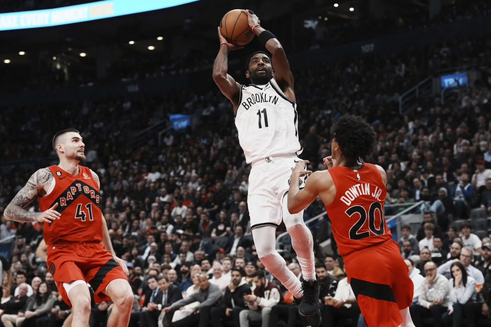 El base de los Nets de Brooklyn Kyrie Irving anota superando al base Jeff Dowtin Jr. y al alero Juancho Hernangomez de los Raptors de Toronto en el encuentro del miércoles 23 de noviembre del 2022. (Chris Young/The Canadian Press via AP)