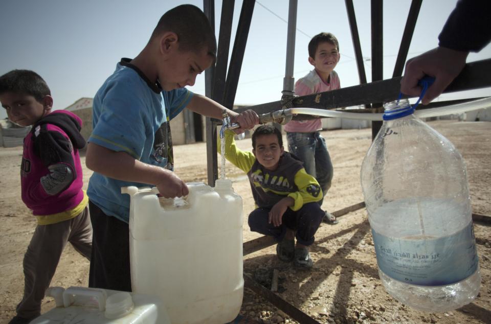 In this Thursday April 17, 2014 photo, Syrian boys fill containers with drinking water at Zaatari refugee camp, near the Syrian border in Jordan. (AP Photo/Khalil Hamra)