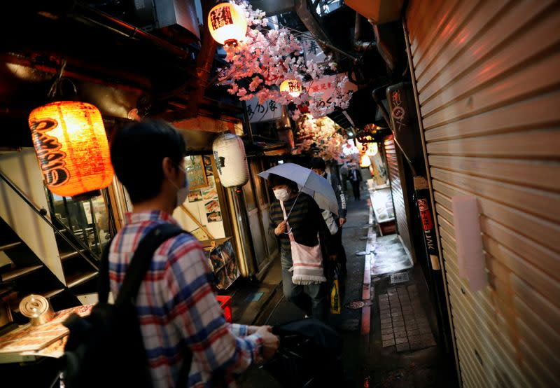 People wearing protective face masks, following the outbreak of the coronavirus disease (COVID-19), walk past the partially reopened Japanese drinking bars alley, in Tokyo