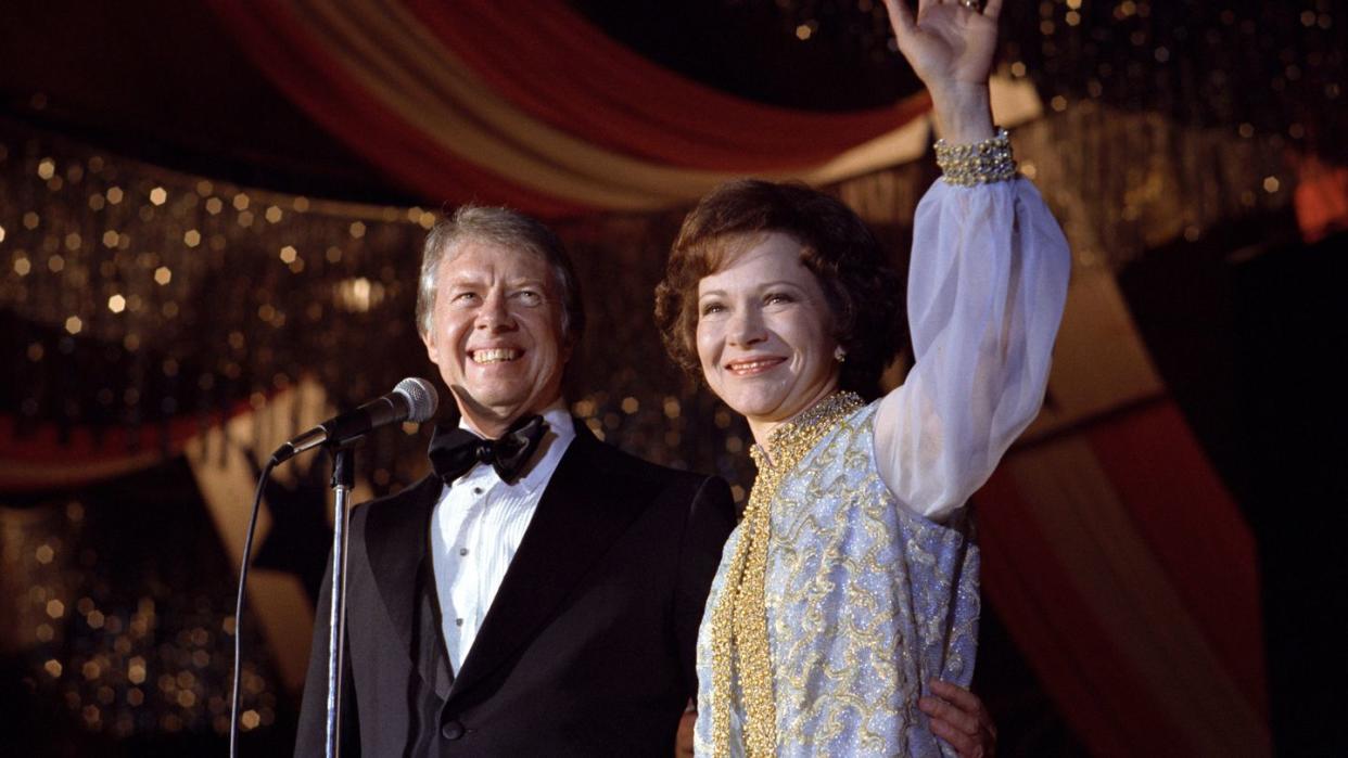 a man and woman standing at a microphone with a red and white flag behind them