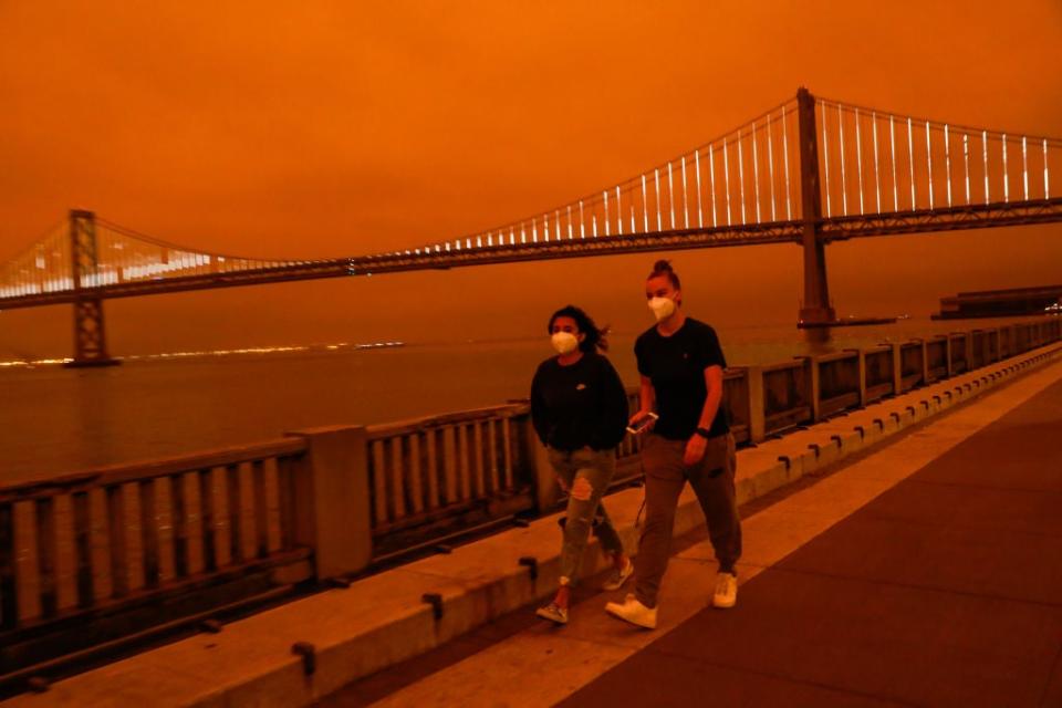 File: People pass by the Bay Bridge as dark orange skies, from wildfire smoke, hang over downtown San Francisco, Calif.