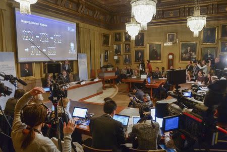 Members of the media listen as professor Claes Gustafsson (standing by the screen), a member of the Nobel Assembly, explains during a news conference at the Royal Swedish Academy in Stockholm October 7, 2015. REUTERS/Fredrik Sandberg/TT News Agency