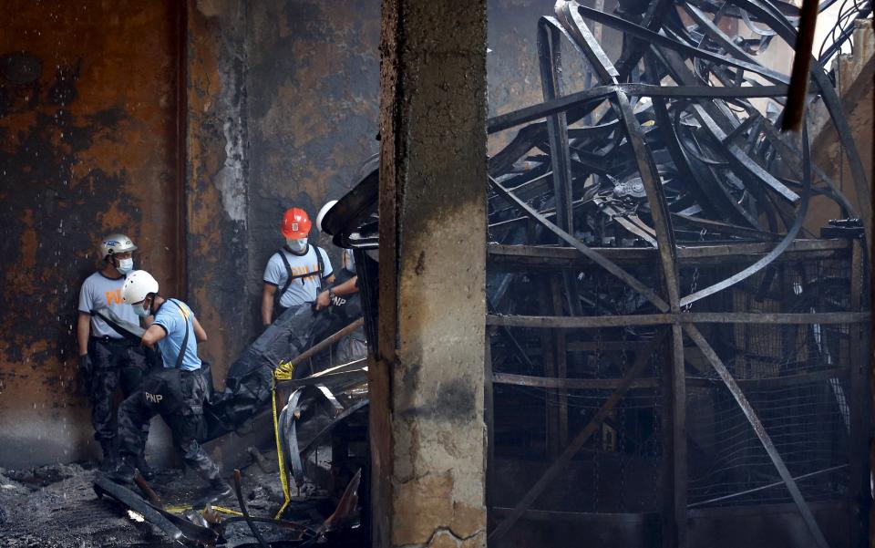 Police carry a body bag containing a body of a worker amidst debris inside a gutted slipper factory in Valenzuela, Metro Manila in the Philippines May 14, 2015.A fire at a factory making rubber slippers killed 31 workers in the Philippine capital on Wednesday, and dozens were missing and feared dead, officials said. REUTERS/Erik De Castro