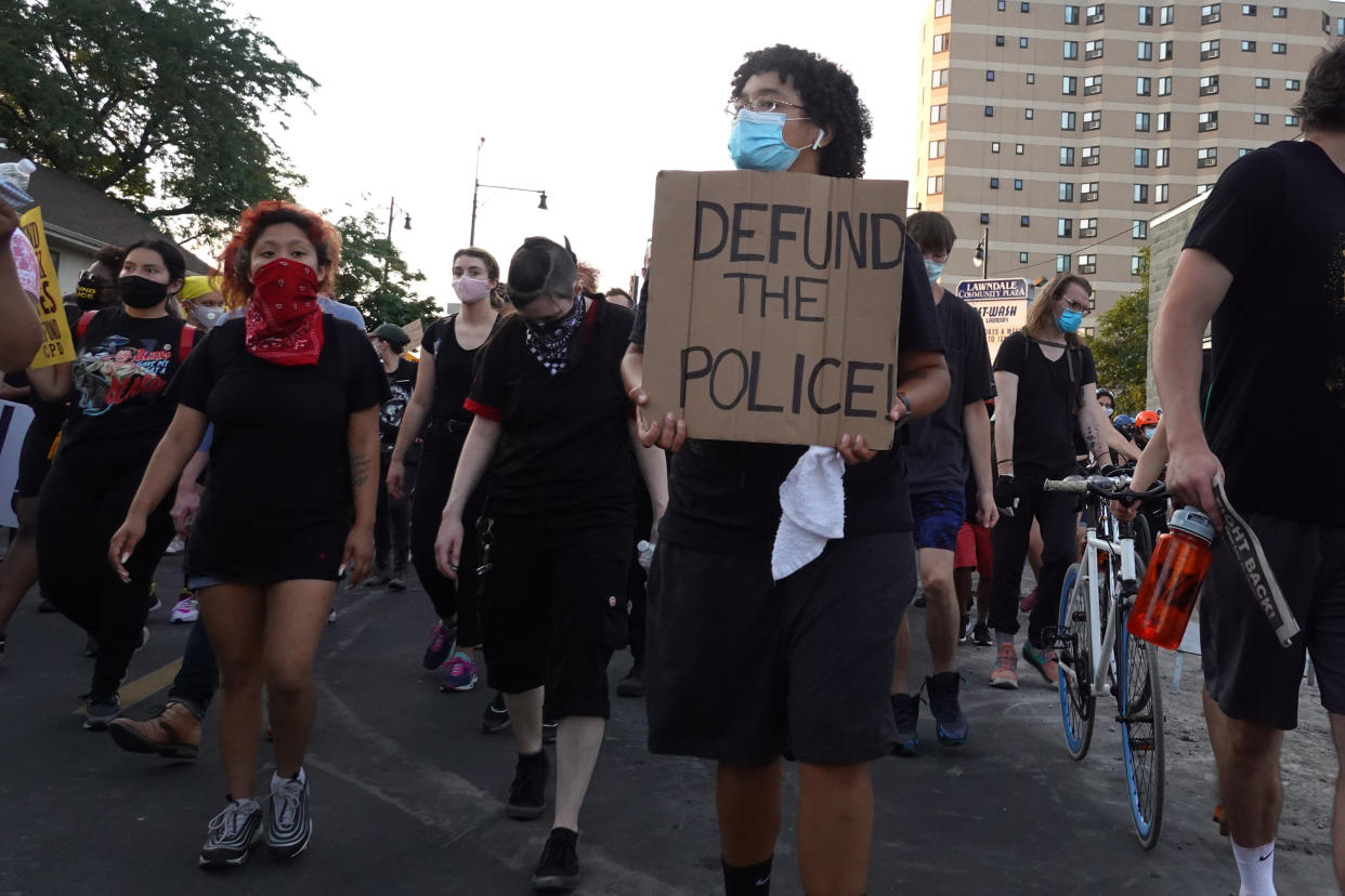Young activists wearing masks march holding signs saying: Defund the Police.