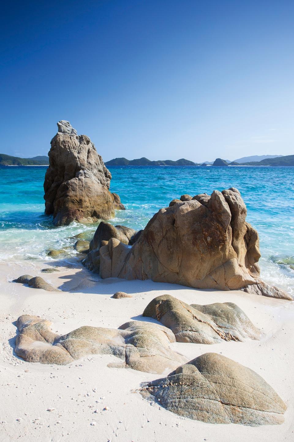 Rock formations standing on a white sand beach with clear turquoise waters