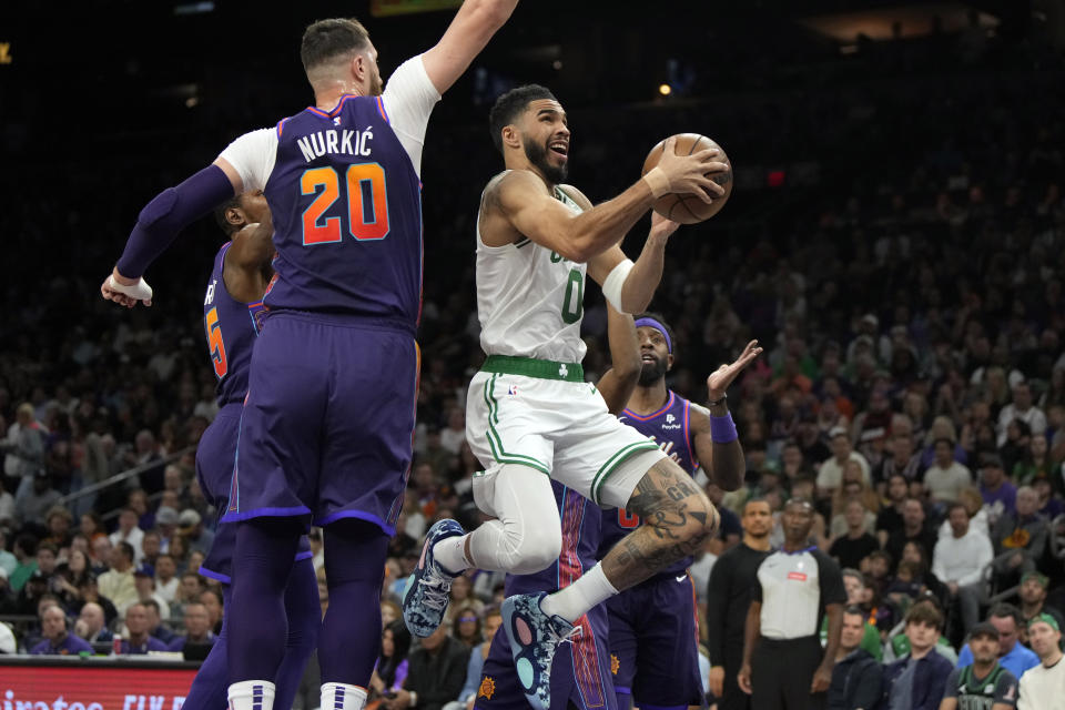 Boston Celtics forward Jayson Tatum (0) drives between Phoenix Suns forward Kevin Duran, left, Jusuf Nurkic (20), and forward Royce O'Neale, right, during the first half of an NBA basketball game, Saturday, March 9, 2024, in Phoenix. (AP Photo/Rick Scuteri)