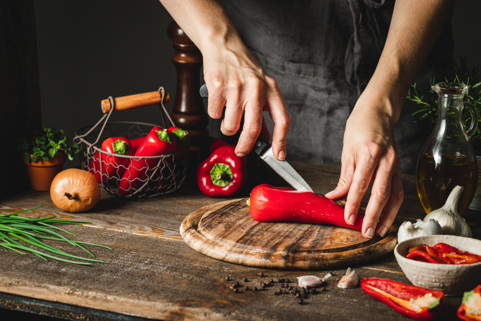 Frau schneidet eine rote Paprika mit einem Messer auf einem Schneidebrett