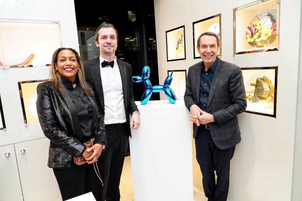 A woman and two men stand around a blue sculpture of a balloon dog