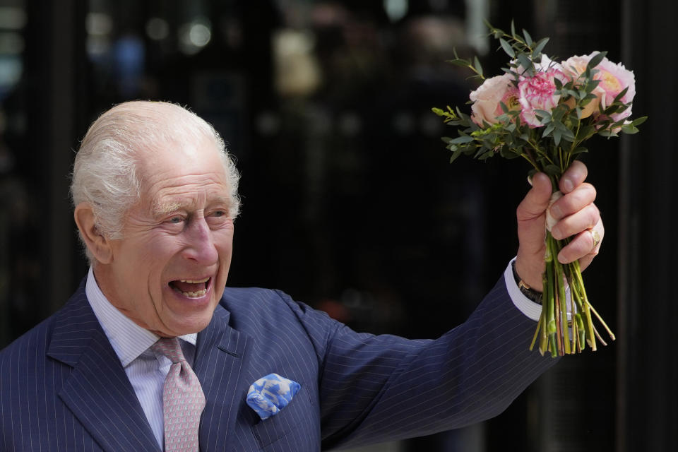 FILE - Britain's King Charles III holds up flowers he was given as he leaves after a visit to University College Hospital Macmillan Cancer Centre in London, Tuesday, April 30, 2024. King Charles III’s decision to be open about his cancer diagnosis has helped the new monarch connect with the people of Britain and strengthened the monarchy in the year since his dazzling coronation at Westminster Abbey. (AP Photo/Kin Cheung, File)